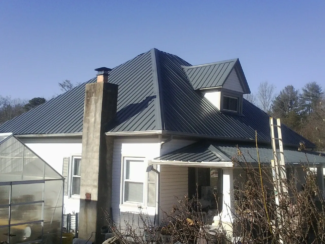 Dark blue standing seam metal roof on a white farmhouse with dormer — Slate & Tile Roof Repair by Roofing Brothers in Seguin