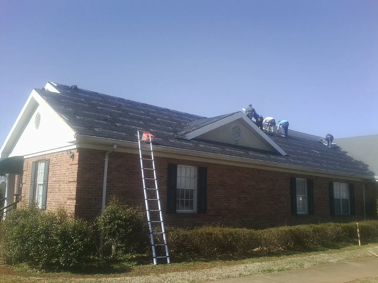 Crew tearing shingles off a brick ranch roof with a ladder set — Metal Roof Repair work by our crew in Seguin