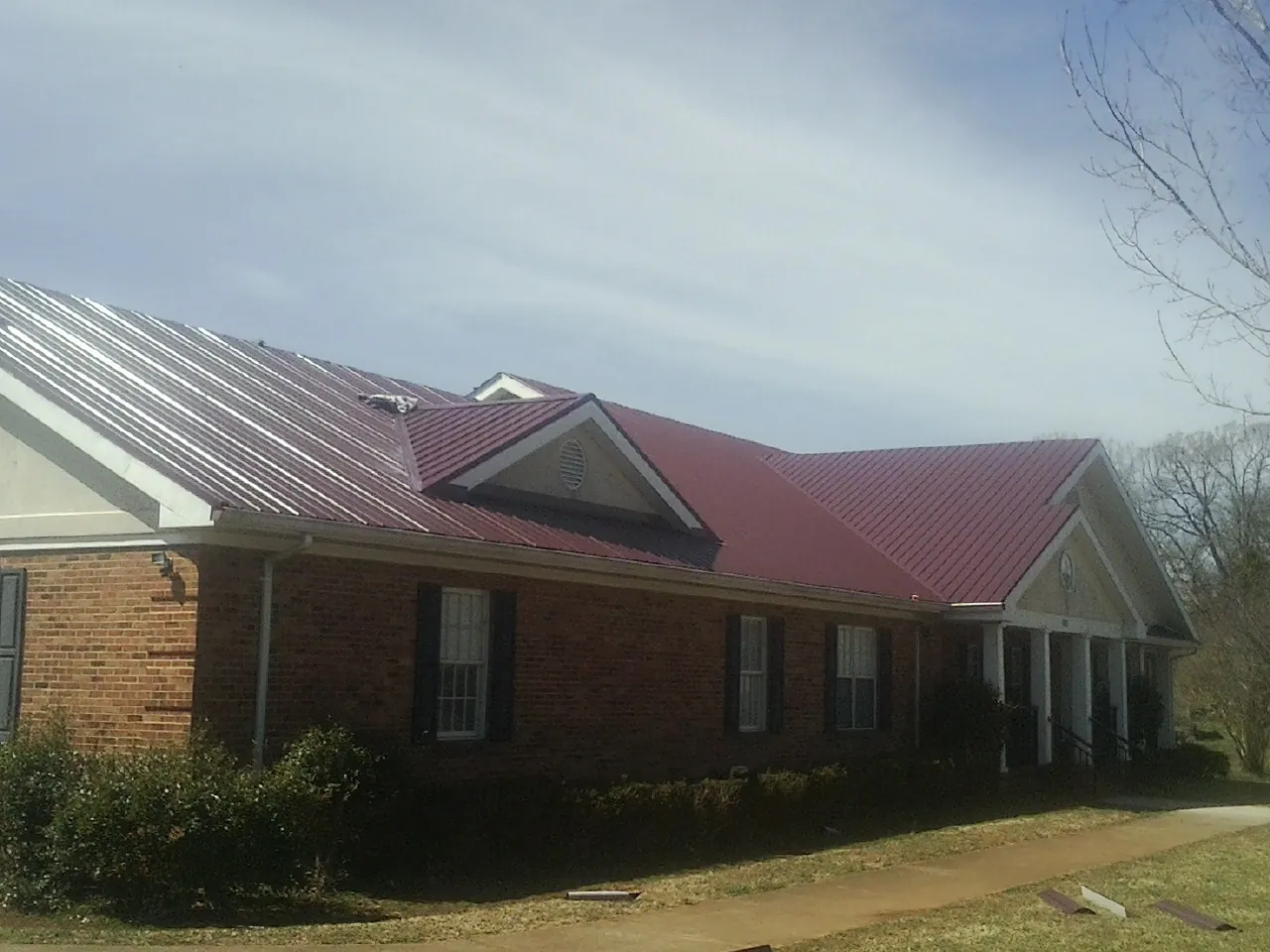 Red metal roof with gabled entries on a long brick building, from a Hail Damage Roof Repair job in Seguin