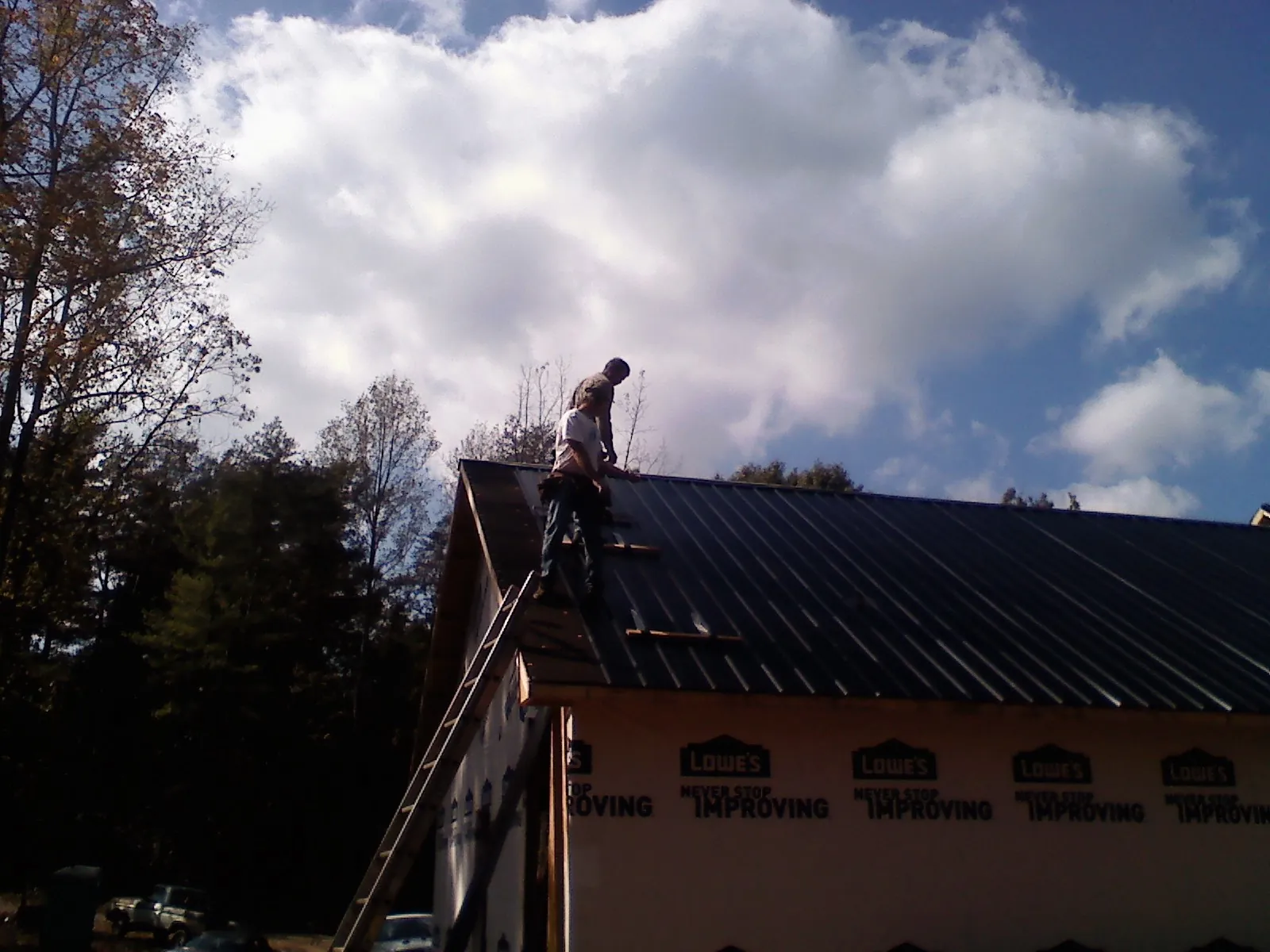 Roofer fastening dark metal panels high against a cloudy sky, from a Roof Inspection job in Seguin