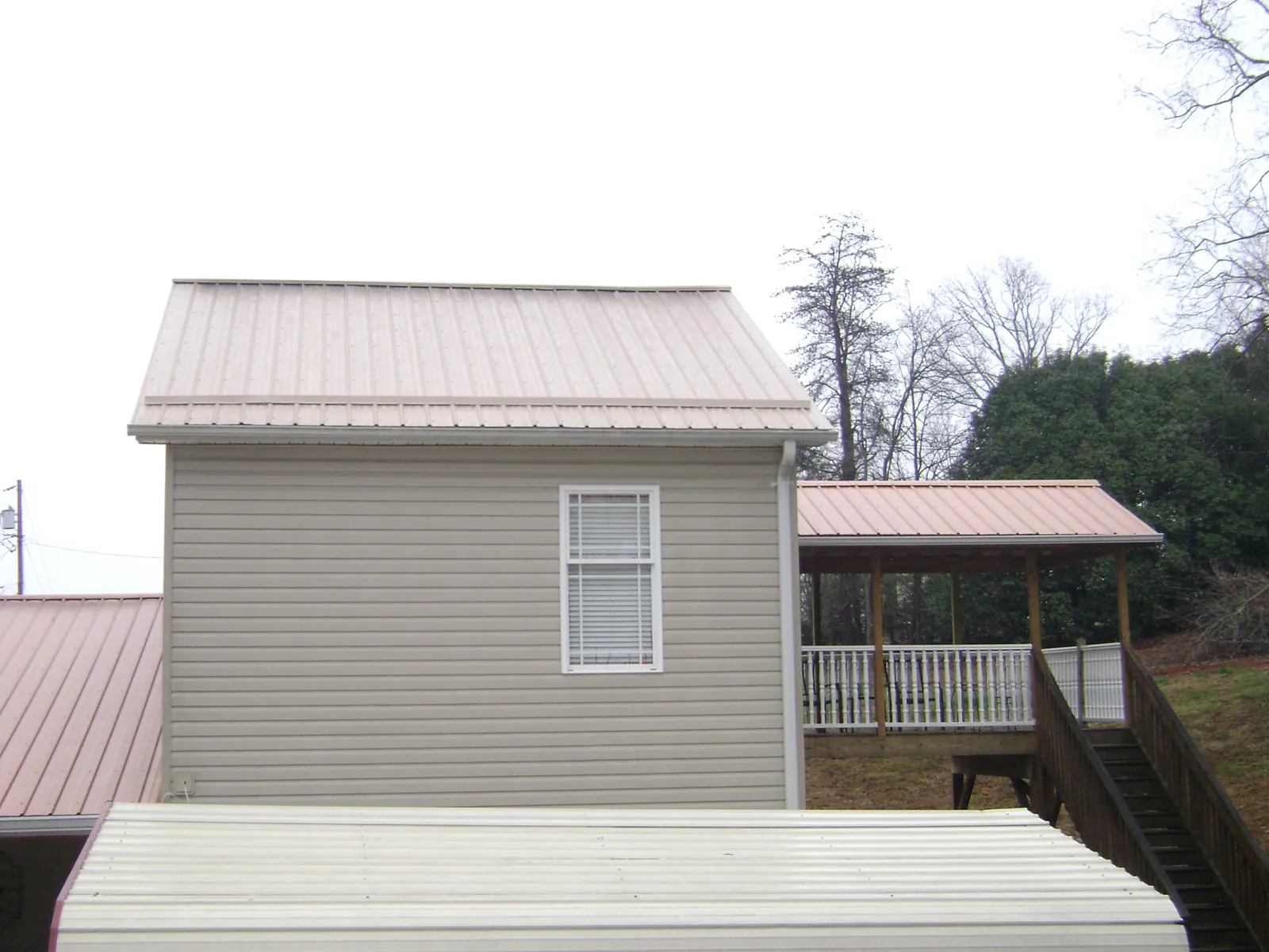 Tan metal roofs on a two story addition and attached porch, from a Roof Replacement job in Seguin